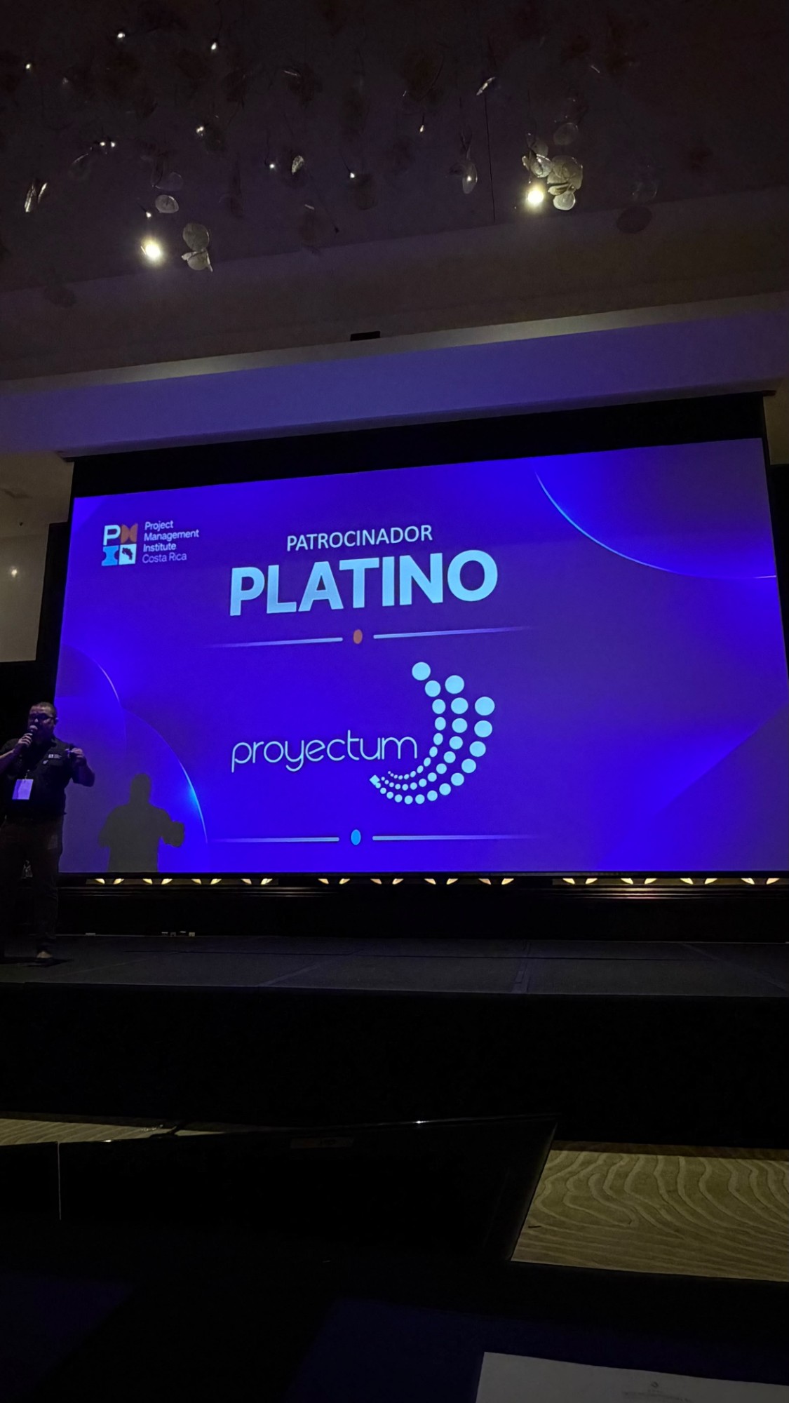 Pantalla del salón principal con el rótulo Patrocinador Platino y el logo de Proyectum